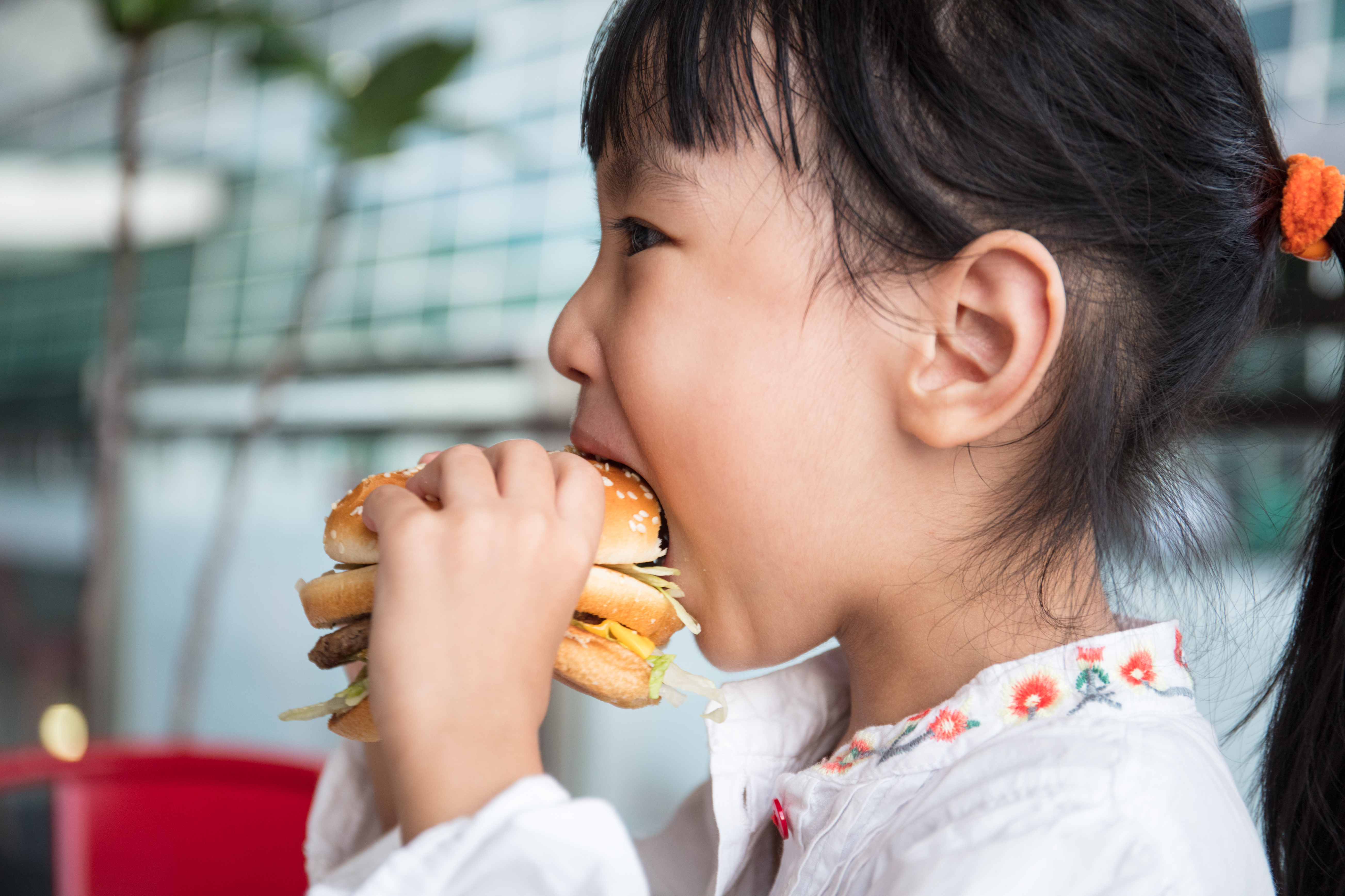 Asian Chinese little girl eating burger at outdoor cafe