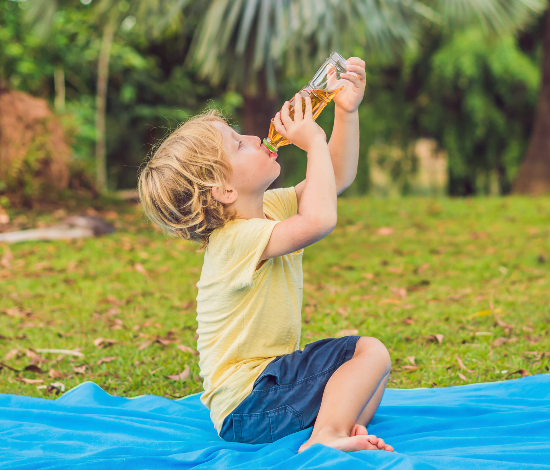 A boy drinks lemonade, tea, kombucha, an orange drink in the park.